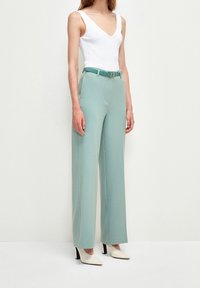 Jasnoniebieskie spodnie typu wide-leg o gładkiej fakturze, z pasującym paskiem i bocznymi kieszeniami, w zestawie z dopasowanym białym topem na ramiączkach i szpilkami.