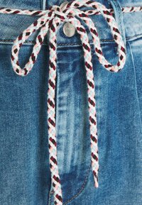 Tessuto denim blu con coulisse intrecciata caratterizzata da motivi rossi, neri e rosa, fissata con un fermo argentato.