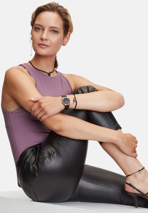 Haut sans manches violet, leggings en simili cuir noir, montre en argent et accessoires, avec une texture lisse et une silhouette ajustée.