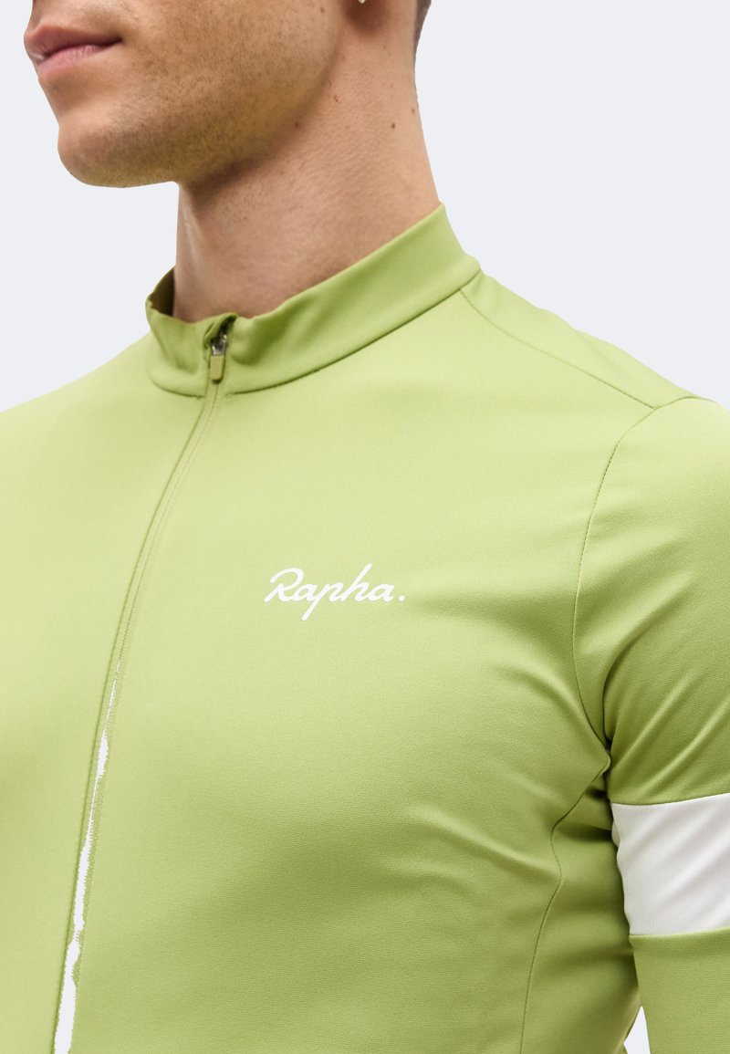 Mann trägt ein hellgrünes Radtrikot mit weißem Streifen am Arm und „Rapha“-Logo auf der Brust, bis zum Kragen zugezogen.