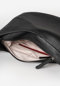 Borsetta nera in pelle con zip, dotata di una leggera fodera interna a motivo e di una piccola tasca interna con zip rossa, mostrata aperta su una superficie bianca.