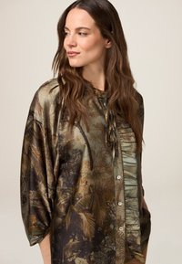 Jedwabna koszula z nadrukiem inspirowanym naturą w ziemistych odcieniach, z zapięciem na guziki z przodu, marszczonymi detalami i szerokimi rękawami.