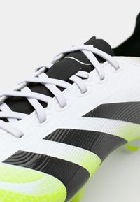 White soccer cleat with black accents and three black stripes, textured upper, thin laces, and a vibrant yellow sole.