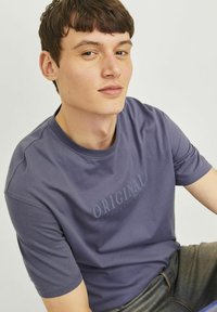Fialové bavlněné tričko s krátkými rukávy a kulatým výstřihem, na přední straně s textem "ORIGINAL" v kontrastním stylu.