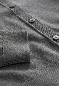 Gros plan d'un cardigan gris en maille avec des poignets côtelés et une patte boutonnée présentant trois boutons gris.