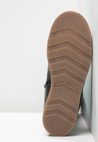 Suela de zapato de cuero negro con un patrón en zigzag. La suela es de goma marrón con ranuras texturizadas para mayor tracción.