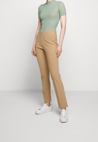 Light green ribbed short-sleeve top paired with tan high-waisted pants featuring side seams; white sneakers completing the outfit.