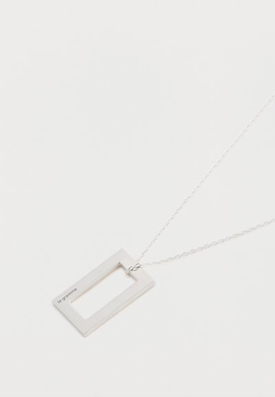 Srebrna pravokotna obesek verižica z odprtim središčem, ki ima tanko verigo in vgravirano besedilo "le gramme." Minimalističen dizajn.