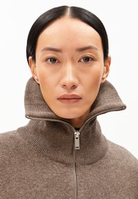 Brun zip-up tröja med hög, ribbad krage och slät textur. Har en silverfärgad dragkedja framtill.