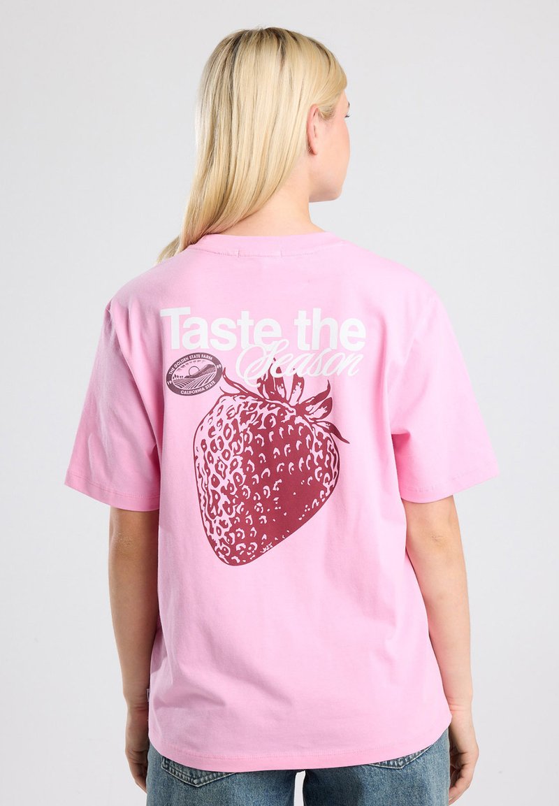 Pink cotton t-shirt featuring a large strawberry graphic in dark red with white text reading "Taste the Season" on the back.