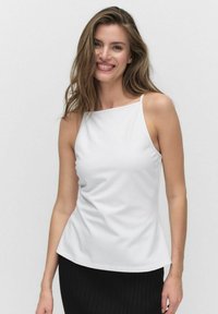 Witte mouwloze top met een gladde textuur, ronde halslijn en vloeiende design. Gecombineerd met een zwarte geribbelde rok.