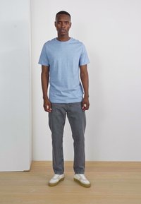 T-shirt à manches courtes bleu clair, jeans gris et baskets blanches avec semelles beige. Design simple, coupe décontractée, texture de tissu lisse.