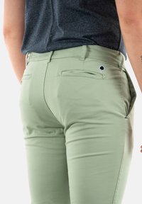 Pantalon vert clair avec une coupe slim, fabriqué en tissu lisse ; il comporte deux poches arrière et un petit logo d'arbre au-dessus de la poche droite.