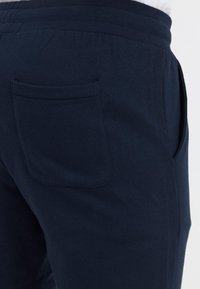 Tmavomodré teplákové nohavice z jemnej bavlny. Majú elastický pás a zadný vrecko so zaobleným okrajom pre elegantný vzhľad.