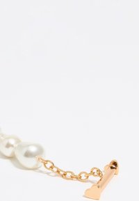 Pulsera de perlas con grandes perlas blancas, enlazadas por una cadena de oro que presenta un cierre de toggles en forma de corazón. Textura suave y brillante.