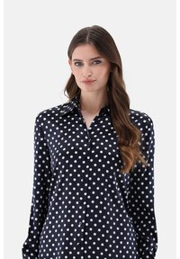 Navy blue, long-sleeve shirt made of smooth fabric featuring a white polka dot pattern and a collared neckline with button closure.