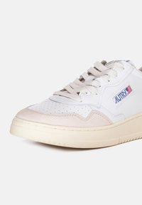 Sneaker bianco e beige con punta perforata, tomaia in pelle liscia, dettagli in suede beige, suola in gomma crema e lacci. Presenta il logo sul lato.