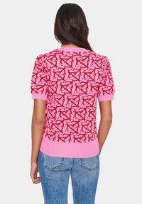 Short-sleeve knit top in pink featuring a red abstract pattern, crew neckline, and fitted hem. Soft texture with ribbed cuffs.