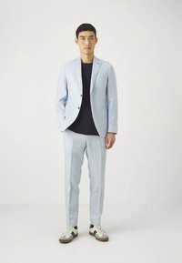 Lichtblauw pak met een op maat gemaakte blazer en bijpassende broek. Draagt een zwart shirt, gecombineerd met witte sneakers met groene en bruine accenten.