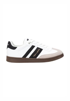 Zapato deportivo blanco con rayas negras, con puntera de ante gris y suela de goma marrón. Cuenta con un diseño de cordones y una marca en el costado.