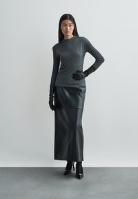 Długa czarna skórzana spódnica zestawiona z dopasowanym, ciemnoszarym topem i czarnymi rękawiczkami. Charakteryzuje się prostą sylwetką z detalami szwów.