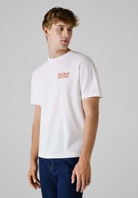 White cotton t-shirt with crew neck and short sleeves, featuring a small orange "Red Bull Racing" logo on the left chest.
