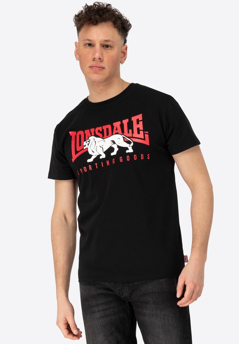 Must mustaga, lühikeste varrukatega must t-särk, mille esiküljel on prinditud punane ja valge "Lonsdale Sporting Goods" logo ja lõvikuju. Pehme puuvillane kangas.