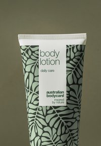 Grön tub med kroppslotion med lövmönster, vit etikett med texten "body lotion daily care", märket "australian bodycare" och texturerad kork.