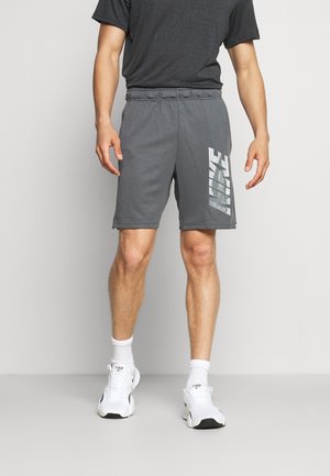 Szare szorty z bocznym odblaskowym logo Nike, elastycznym pasem i luźnym krojem. W połączeniu z czarną koszulką z wzorem i białymi trampkami.