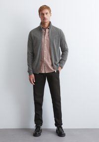 Gray zip-up jacket with high collar over a light pink button-up shirt, paired with dark pants and black shoes. Simple, clean design.