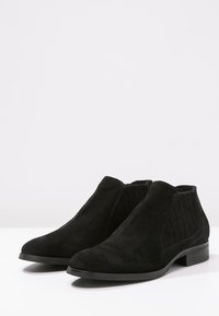 Black suede ankle boots with elastic side panels, low block heel, and a smooth textured finish. Simple, classic design suitable for various styles.