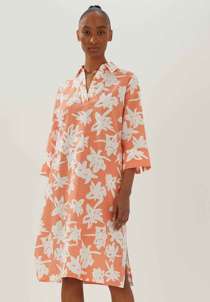 Koraalkleurige linnen jurk met wit bloempatroon, uitgerust met een kraag, driekwart mouwen en zijsplitten voor gemakkelijk bewegen.