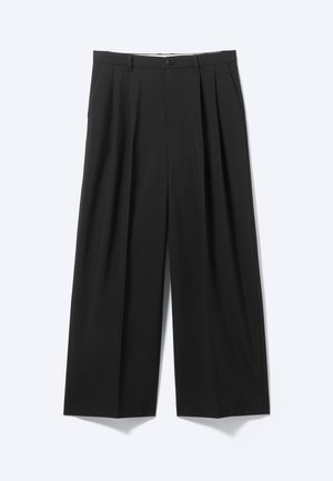 Svarte bukser med vide ben, forklebber foran, beltehemper og knappelukking, vist på en ensfarget lys bakgrunn.