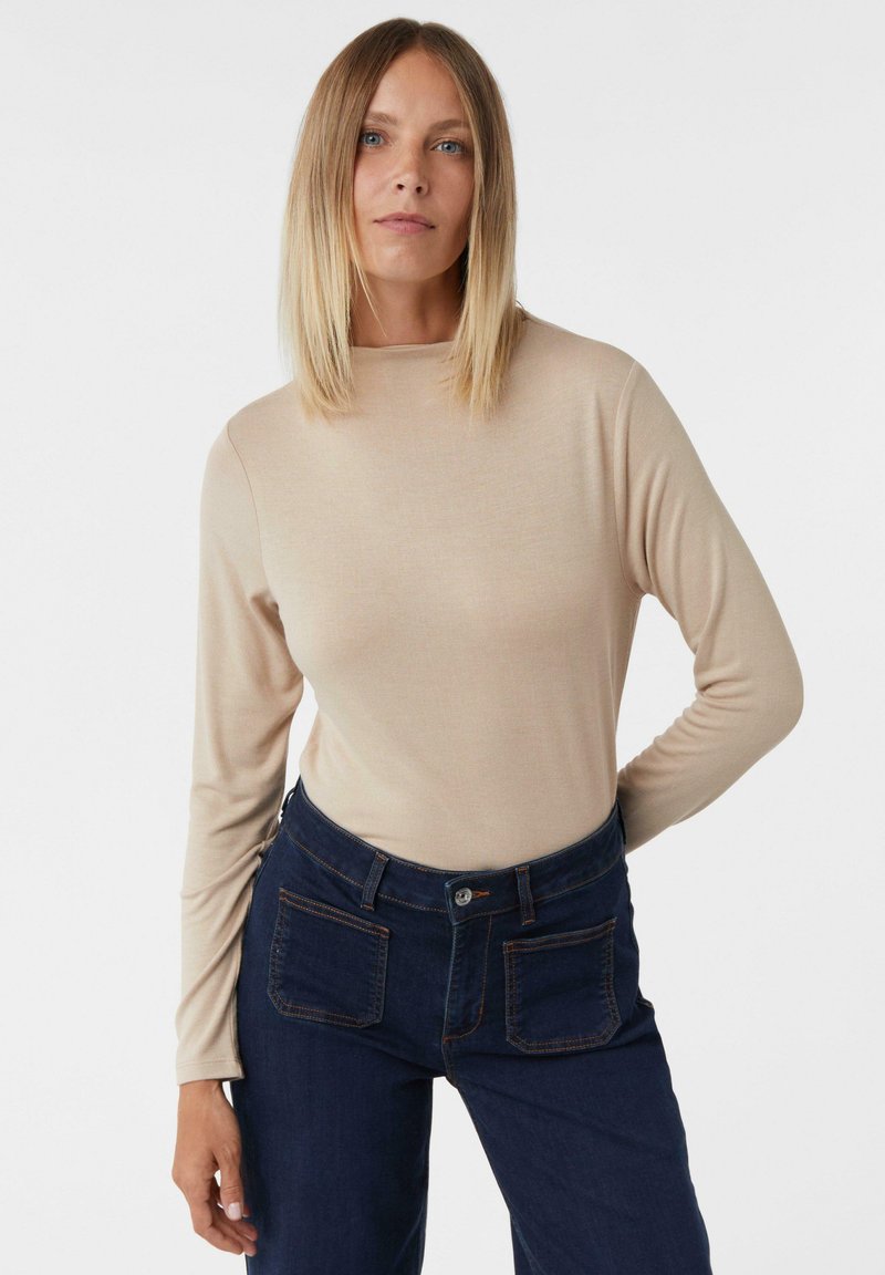 Beige Langarmoberteil aus weichem Stoff mit rundem Halsausschnitt, kombiniert mit dunkelblauen Jeans aus Denim mit kontrastierenden Nähten und Taschen.