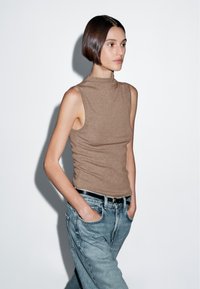Brown sleeveless top with a high neck, paired with light blue denim jeans. The top features a fitted design and soft texture.