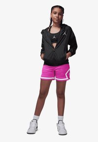 Jachetă neagră cu fermoar, pantaloni scurți sport roz cu accente albe, sutien sport negru și adidași albi cu detalii negre.