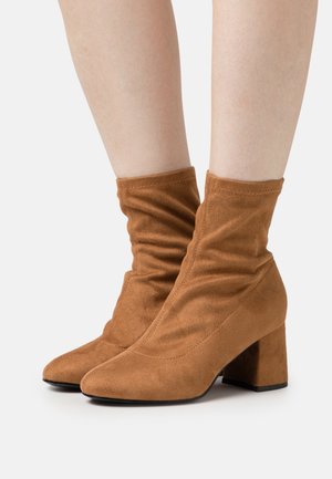 Brown suede ankle boots with a slouchy design, pointed toe, and a chunky heel texture. The upper features stitched detailing.