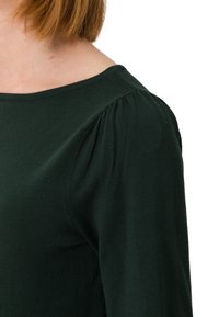 Tummanvihreä neulepaita, jossa on pehmeä rakenne, leveä pääntie ja rypytetty yksityiskohta olkasessa. Tyköistuva siluetti.
