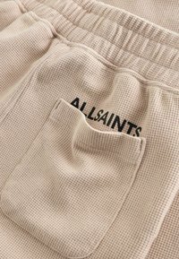 Beežist vahvlilõnga kangas, millel on elastne vöökoht ja tasku, mis osaliselt katab "ALLSAINTS" trükitud teksti.