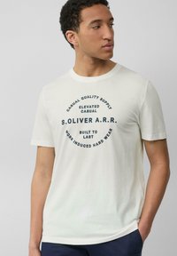 Crème t-shirt met korte mouwen van katoen, met een ronde opdruk in donkerblauwe tekst met de merknaam en slogans in het midden.
