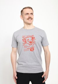 Grå bomull t-shirt med en röd grafik av en leende ko och text. Korta ärmar och en klassisk rund halsringning.