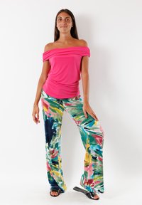 Top rosa scollato con drappeggi, abbinato a pantaloni a gamba larga con un vivace motivo floreale nei toni del verde, rosa e blu. Sandali neri.