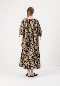Robe maxi en tissu noir avec un motif floral doré, dotée de manches bouffantes et d'une coupe ample, resserrée par des cordons aux épaules.