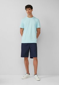 Jasnoniebieska koszulka z krótkim rękawem, zestawiona z granatowymi szortami i białymi trampkami. Prosty wzór, bawełniana tekstura i luźny fason.