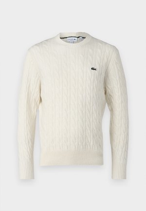 Cream cable-knit sweater with a round neckline, ribbed cuffs and hem, and a green Lacoste logo on the chest. Textured fabric enhances detail.