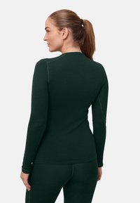 Donkergroen top met lange mouwen en een gladde textuur, voorzien van platte naden en een aansluitend ontwerp, gecombineerd met bijpassende legging.