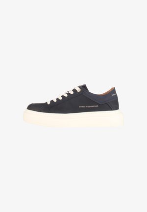 Zwarte lage sneaker met witte veters en dikke witte zool, met "Alexander Smith" branding op de zijkant en hielkraag.