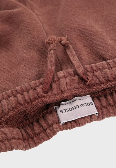 Primer plano de una cinturilla de tela marrón con cordón y etiqueta de ropa blanca que muestra el nombre de la marca "Bobo Choses".