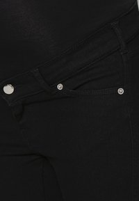 Os jeans de ganga pretos apresentam um design clássico de cinco bolsos com ferragens prateadas e uma textura suave. O tecido possui um ligeiro brilho.