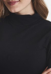 Sort rullekrave top lavet af blødt, strækbart stof, med et tætsiddende design og glat tekstur samt forstærkede sømme.